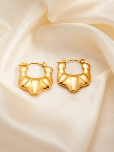 Detail of gold croissant hoop earrings with textured finish on elegant beige silk background