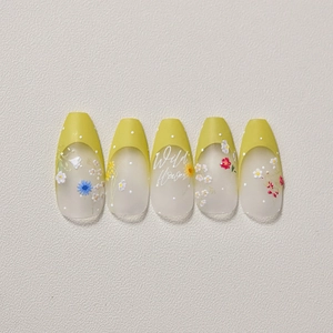 Détail d'ongles mats coffin avec pointes French jaunes et motifs de fleurs sauvages
