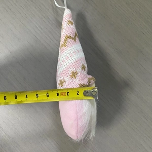 Gnomo natalizio in maglia rosa misurato con un metro a nastro giallo su legno