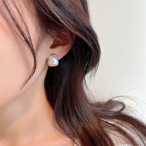 Close-up of geometric square stud earring with iridescent finish and gold frame on ear