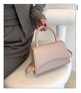Close-up of beige crocodile pattern bag with woven handle and gold metal hardware