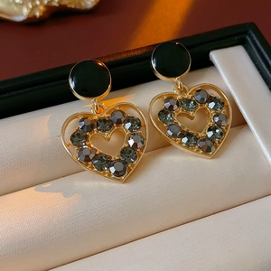 Détail de boucles d'oreilles cœur dorées avec touches noires sur coussin velours beige