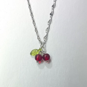 Silver necklace with a red cherry pendant and green leaf charm on a clean grey background