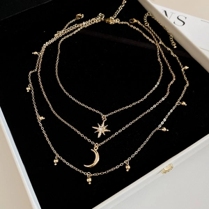 Detail of layered gold necklace with diamond star and crescent moon pendants in a jewelry box