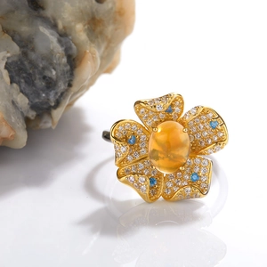Macro detail of a golden flower ring with orange oval gemstone and blue accent diamonds