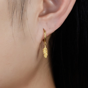 Macro view of gold feather pendant hoop earrings worn by model showing texture