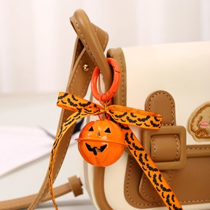 Cute Halloween pumpkin bell keychain accessory hanging on a brown crossbody bag