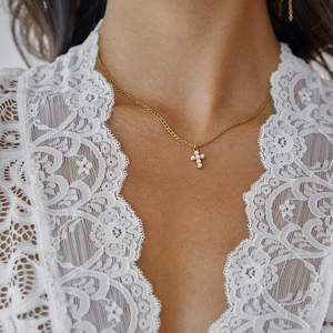 Close-up of a gold cross pendant necklace with pearls worn on a female model neck