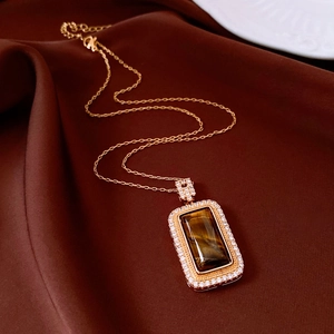 Macro shot of rose gold necklace featuring tiger eye stone pendant on brown silk
