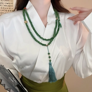 Détail d'un long collier de perles vertes avec agate rouge et pompon en soie