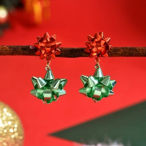 Festive red and green metal bow earrings hanging on a branch with holiday bokeh
