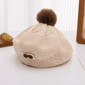 Detail view of beige cable knit beret with brown pompom and small bow accent