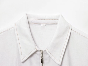 Détail rapproché de la veste en coton sergé blanc avec surpiqûres brunes et fermeture éclair
