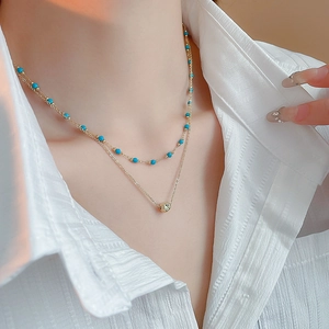 Detail view of double-layered gold necklace with blue beads and geometric pendant