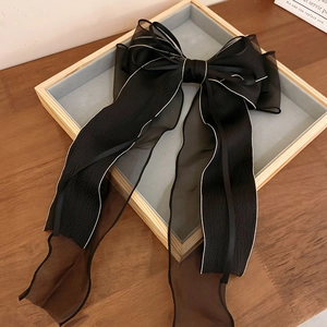 Detail of elegant black lace bow hair clip with long ribbons and white contrast piping