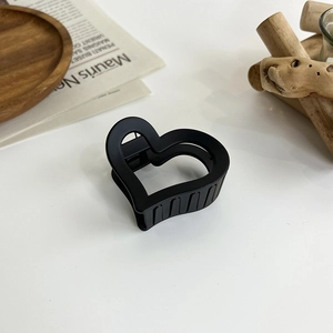 Close-up of matte black heart-shaped hair claw clip on minimalist wooden decor