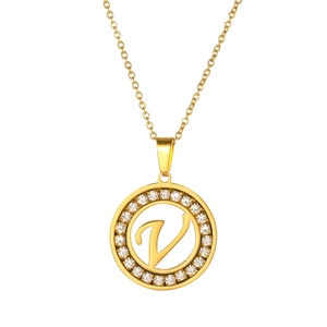 Detail of a gold-plated circular pendant with V-letter and shimmering crystal inlay