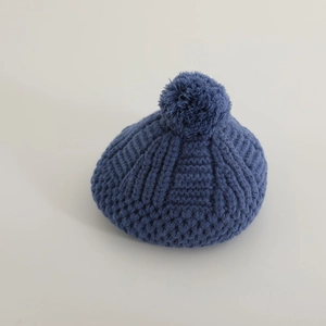 Détail du tissage en maille et du pompon sur le béret bleu foncé pour fille en hiver