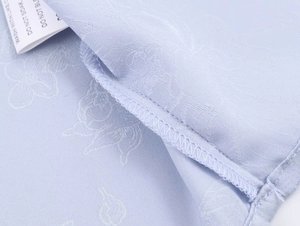 Detailansicht von hellblauem Jacquard-Stoff mit Nähten und dem Pflegeetikett