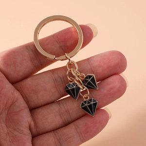 Detail of three black enamel diamond pendants on a rose gold keychain held by a hand