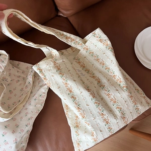 Floral cotton canvas tote bag with orange floral print and woven label on a sofa