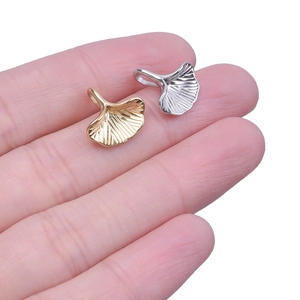 Close-up of gold and silver ginkgo leaf pendants held to show actual size and texture