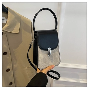 Detail of a chic two-tone leather handbag with silver clasp held against a trench coat