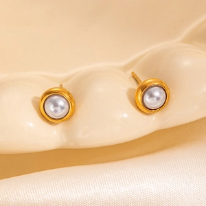 Close-up of elegant pearl stud earrings with gold rim on textured cream ceramic tray