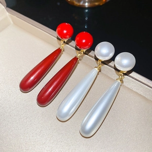 Detailed view of red and pearl white teardrop earrings displayed on beige silk