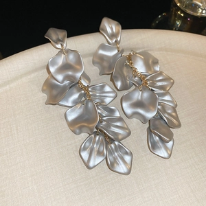 Close-up of matte silver petal drop earrings with gold chain links on a textured tray