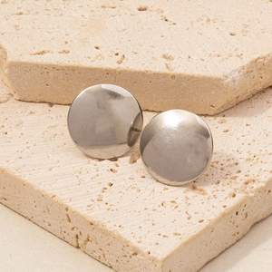 Close-up of polished 304 stainless steel round stud earrings on beige travertine stone