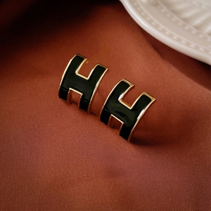 Close-up of elegant H letter gold earrings with black enamel on silk background