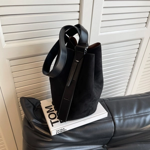 Minimalist black suede bucket bag with adjustable leather strap on a white book