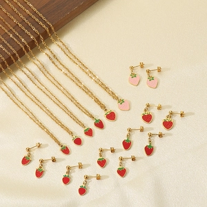 Detailed view of gold titanium strawberry necklaces and earrings set on beige fabric
