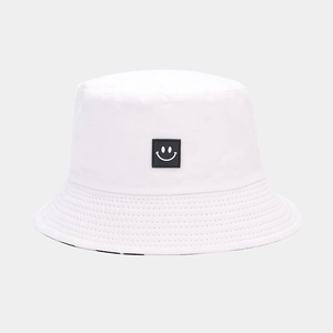 Detailed view of white cotton bucket hat featuring a black square smiley face patch