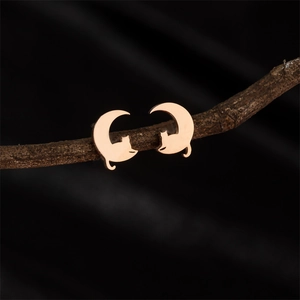 Close-up of rose gold cat silhouette earrings hanging on a natural wooden branch