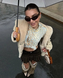 Street style shot of a beige faux fur jacket paired with a brown pleated mini skirt and boots