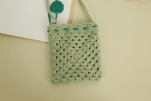Close-up of light green hand-crocheted bag with hollow pattern and heart tassel