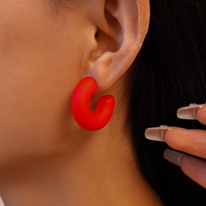 Detail of red matte acrylic chunky C-shaped hoop earring on model with elegant style