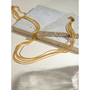 Detail of layered 18k gold snake chains showing texture on beige travertine stone