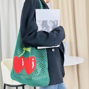 Detail of green knitted tote bag with cherry pattern and mesh texture in a home setting