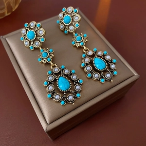 Vintage gold drop earrings with turquoise stones and pearls on a bronze jewelry box