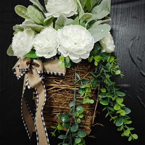 Close-up of white artificial roses and greenery in a woven basket with burlap bow