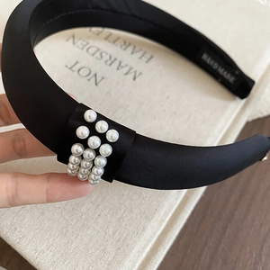 Detail of black satin headband featuring three rows of pearls and handmade textile label