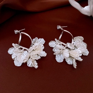 Dettaglio di orecchini d'argento con petali di fiori madreperla su tessuto rosso