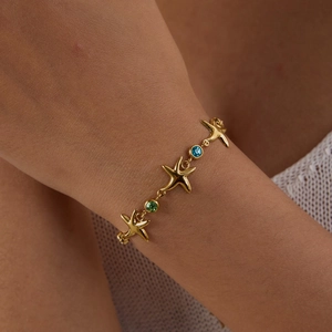 Detail of starfish charm bracelet in gold with blue and green zircons on a woman's wrist
