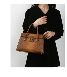 Detail of brown crocodile pattern handbag with gold twist lock and dual top handles