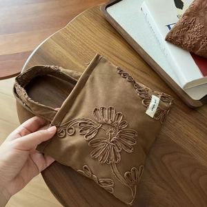 Close-up of vintage brown suede tote bag with embroidered sunflower details and brand tag