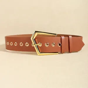 Detail of caramel brown wide leather belt with large golden geometric buckle and metal eyelets