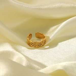 Macro shot of gold textured open ring with rhombus pattern on beige silk background